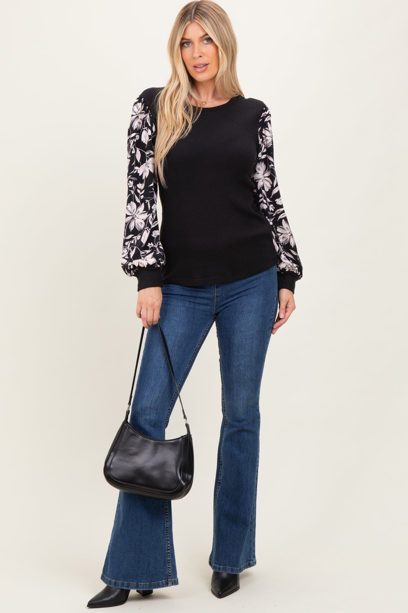 woman wearing a black ribbed sweater with floral patterned sleeves, paired with flared jeans and holding a black handbag