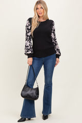 woman wearing a black ribbed sweater with floral patterned sleeves, paired with flared jeans and holding a black handbag