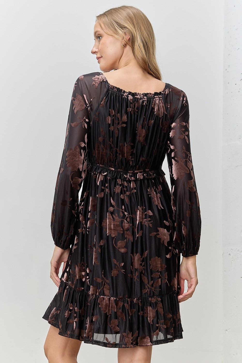 woman wearing a black floral print dress with long sleeves and a tiered hem, view shows the back of the dress