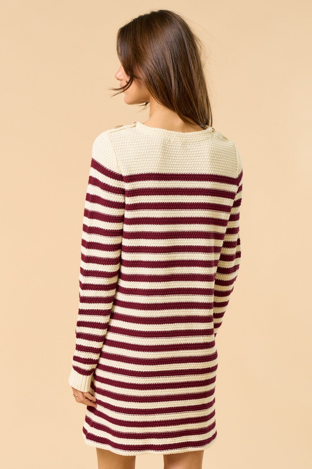 woman wearing a maroon and cream striped knit sweater dress with button details on the shoulders from the back