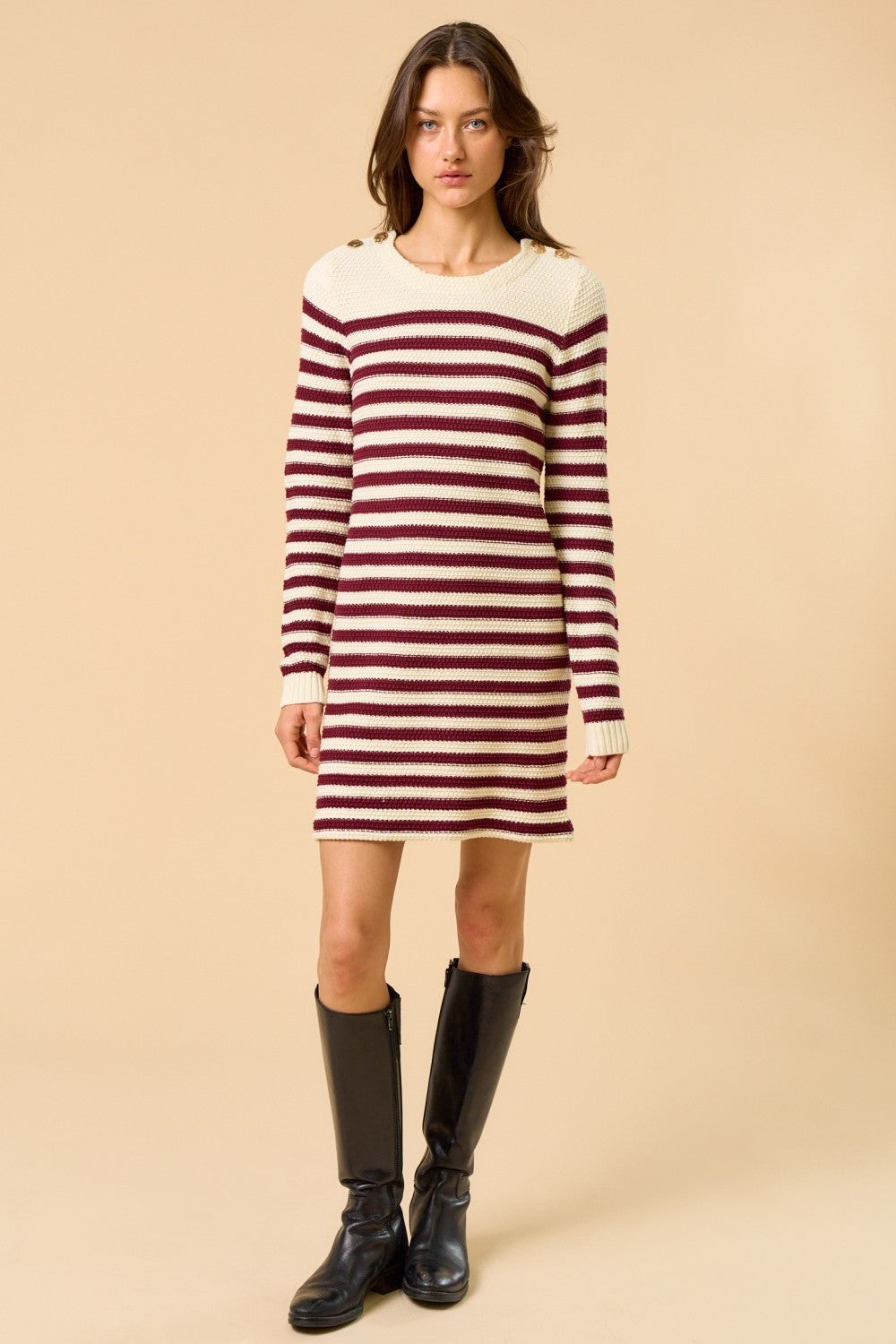 woman wearing a cream and burgundy striped sweater dress with a round neck and long sleeves, paired with knee-high black boots