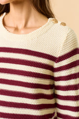 woman wearing a cream and burgundy striped sweater with button details on the shoulder