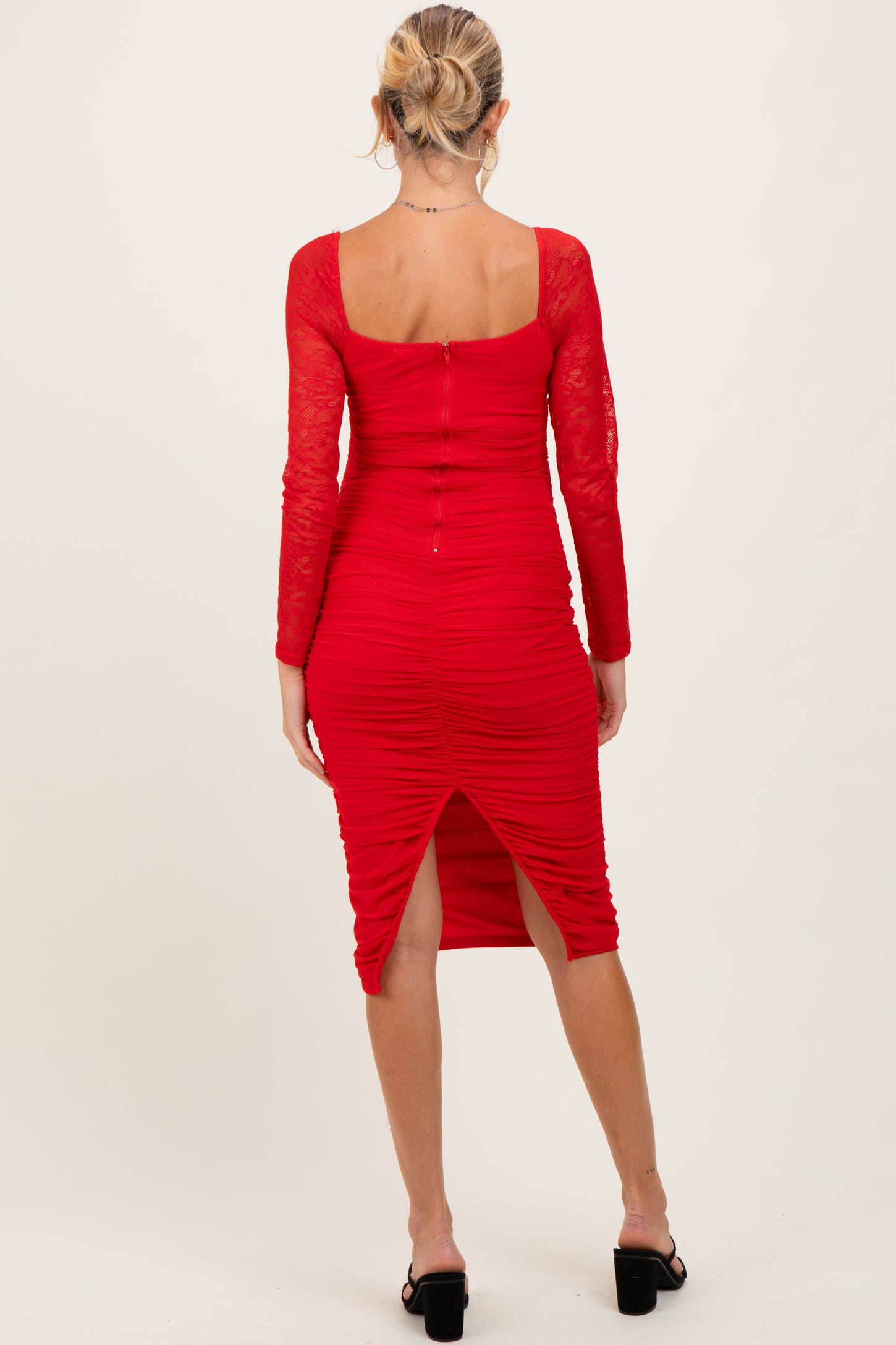 woman wearing a red long sleeve ruched maternity dress with lace sleeves and a back slit