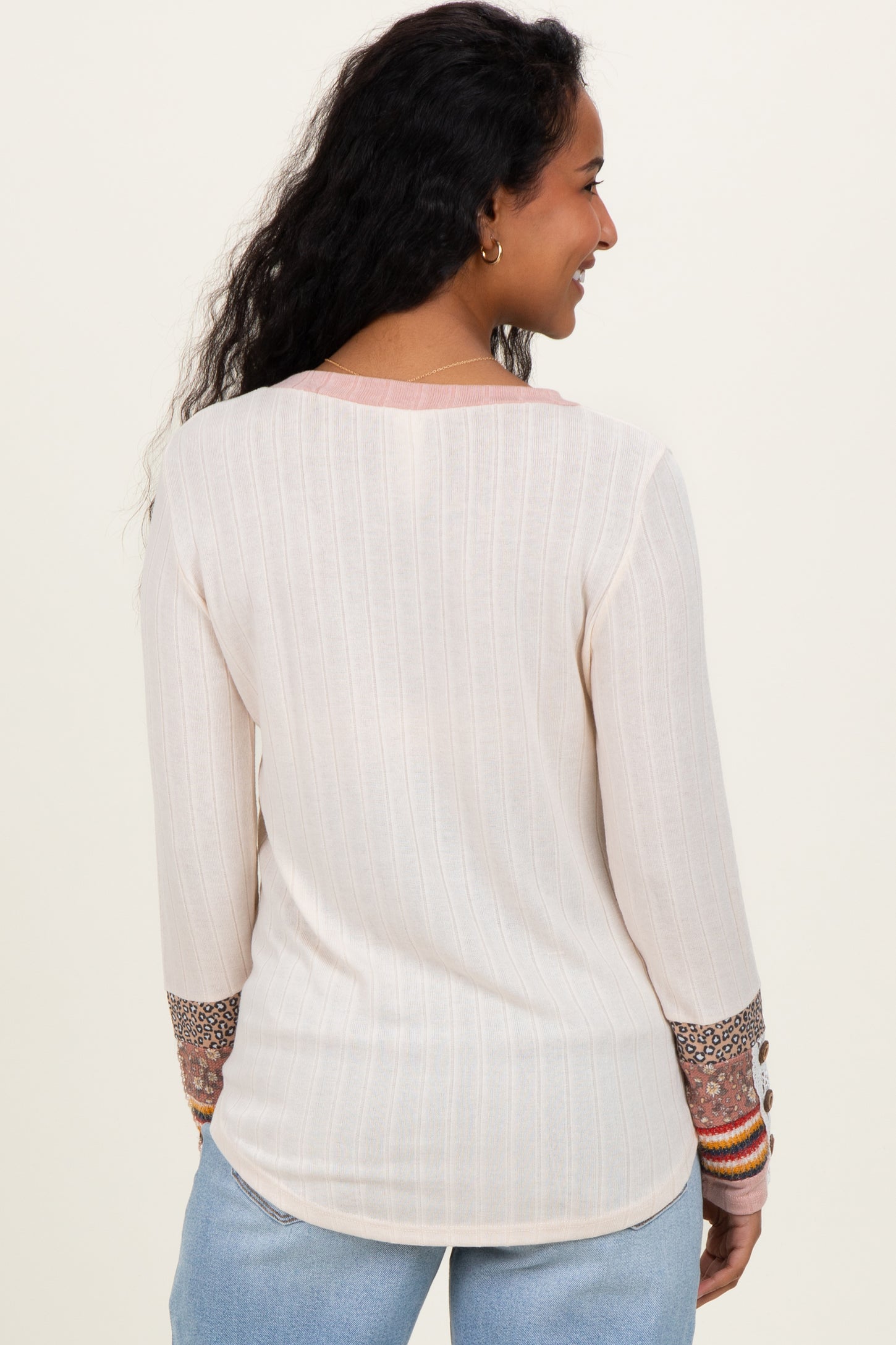 woman wearing a cream long sleeve maternity top with patterned sleeves and a relaxed fit, showing her back