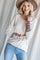 woman wearing a cream ribbed long sleeve top with colorful patterned sleeves and a pink neckline