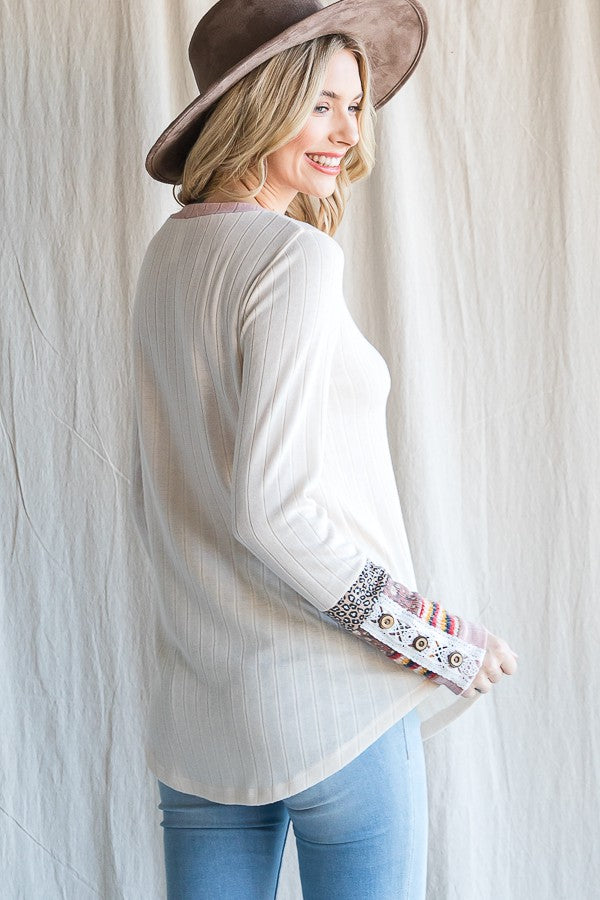 woman wearing a cream long sleeve top with patterned sleeves and a floppy hat, smiling and facing away from the camera