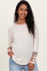 woman wearing a cream ribbed maternity top with colorful patterned sleeve details and a visible baby bump