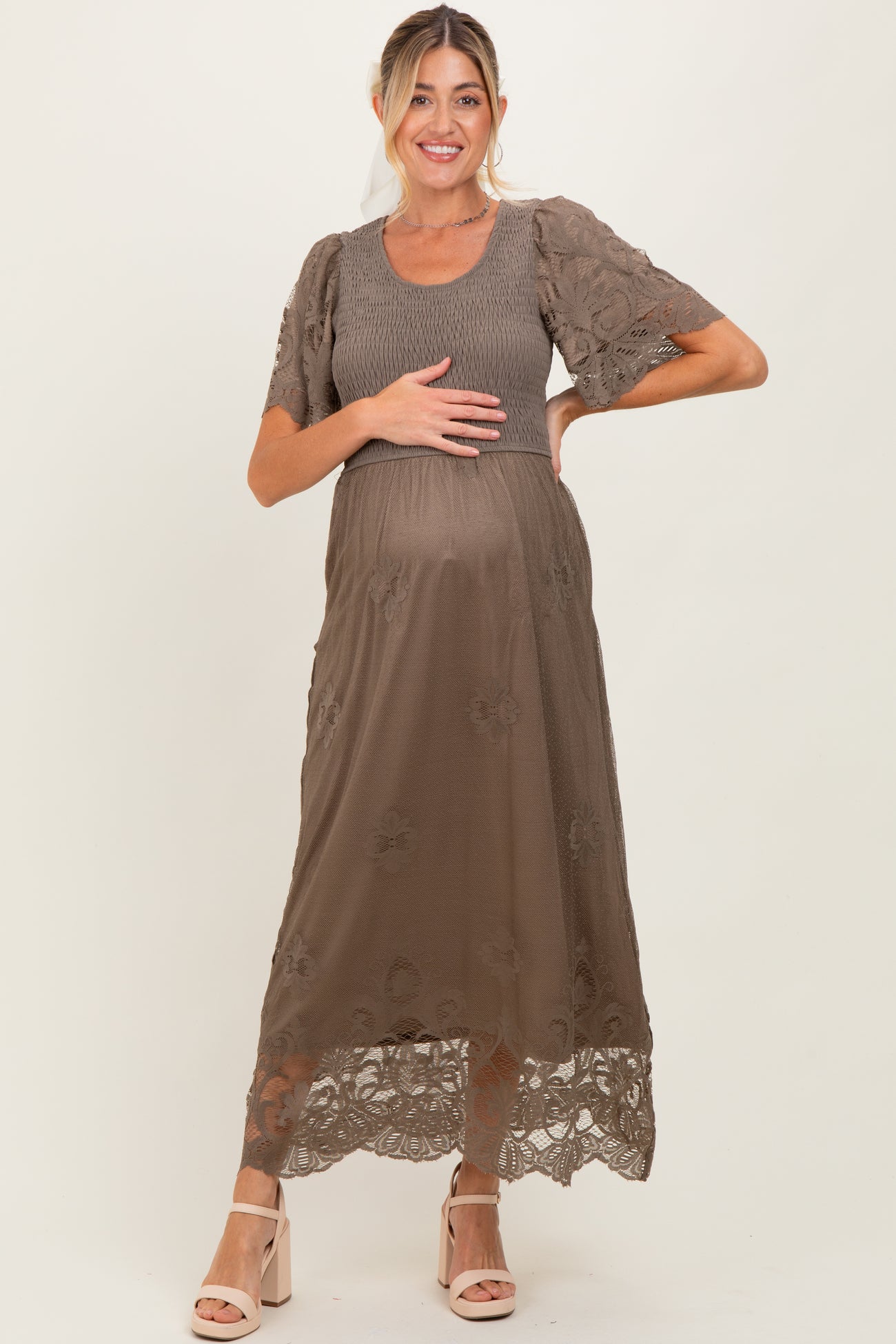 woman wearing a brown maternity dress with floral lace details, holding her baby bump
