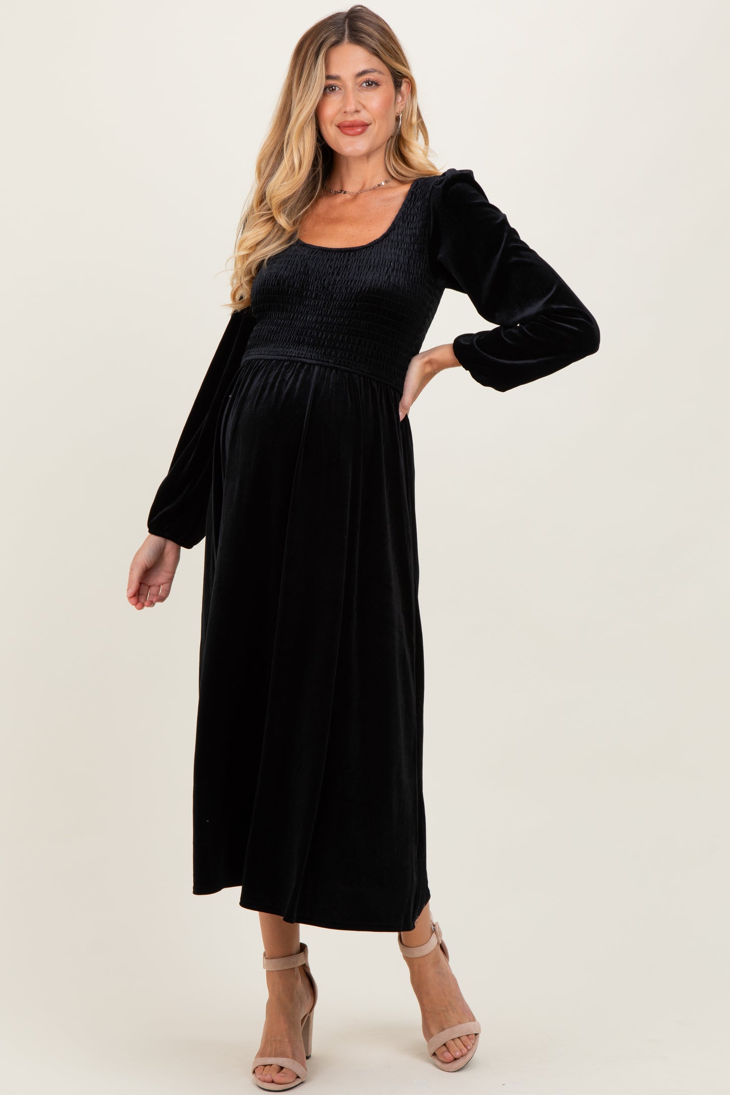 woman wearing a black smocked maternity dress with long sleeves and a fitted bodice, showcasing a baby bump