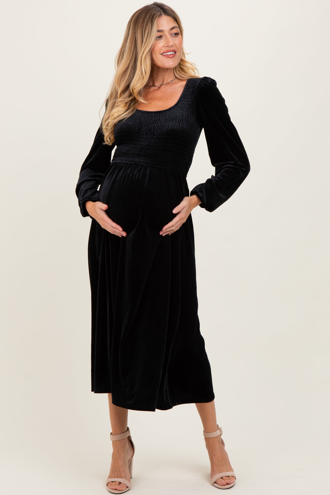 woman wearing a black velvet maternity dress with long sleeves and a smocked bodice, cradling her baby bump
