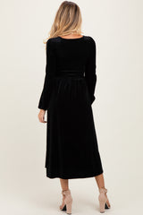 woman wearing a black velvet maternity dress with long sleeves and a flowing skirt, showing off a baby bump from the back