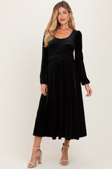 woman wearing a black velvet maternity dress with long sleeves and a fitted bodice, showing a baby bump