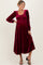 woman wearing a burgundy velvet maternity dress with long puff sleeves and a smocked bodice, showcasing a baby bump