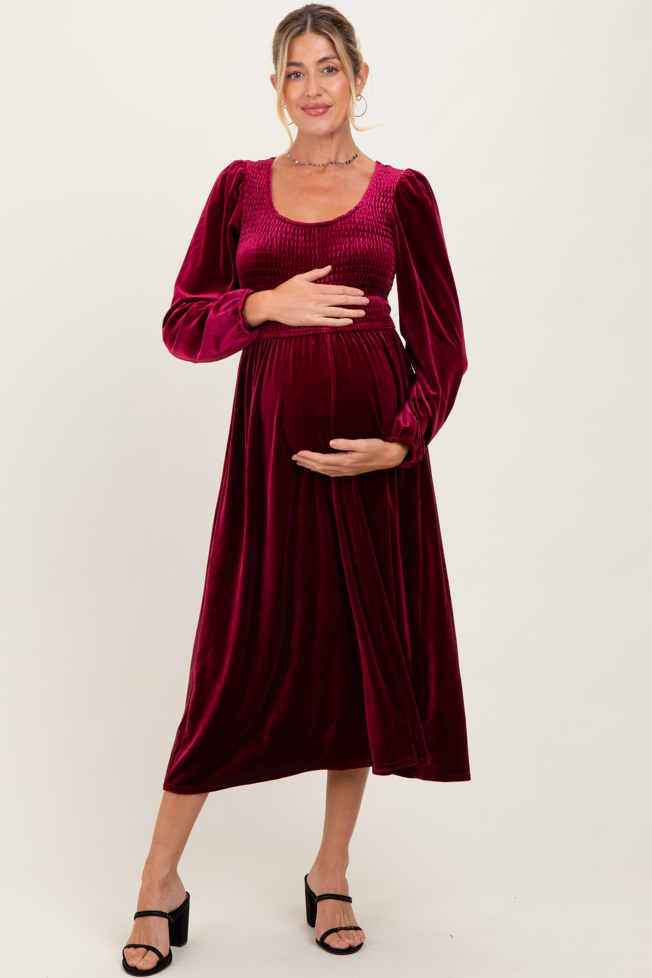 woman wearing a burgundy velvet maternity dress with long puff sleeves and a fitted bodice, cradling her baby bump