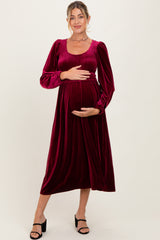 woman wearing a burgundy velvet maternity dress with long puff sleeves and a fitted bodice, cradling her baby bump