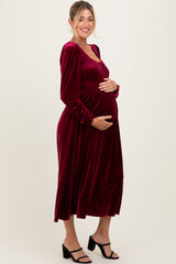 woman wearing a burgundy velvet maternity dress with long sleeves and smocked bodice, holding her baby bump