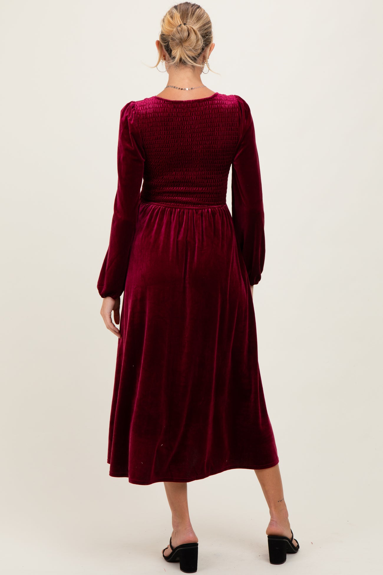 woman wearing a burgundy velvet maternity dress with long sleeves and a smocked bodice, showing the back view