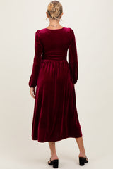 woman wearing a burgundy velvet maternity dress with long sleeves and a smocked bodice, showing the back view