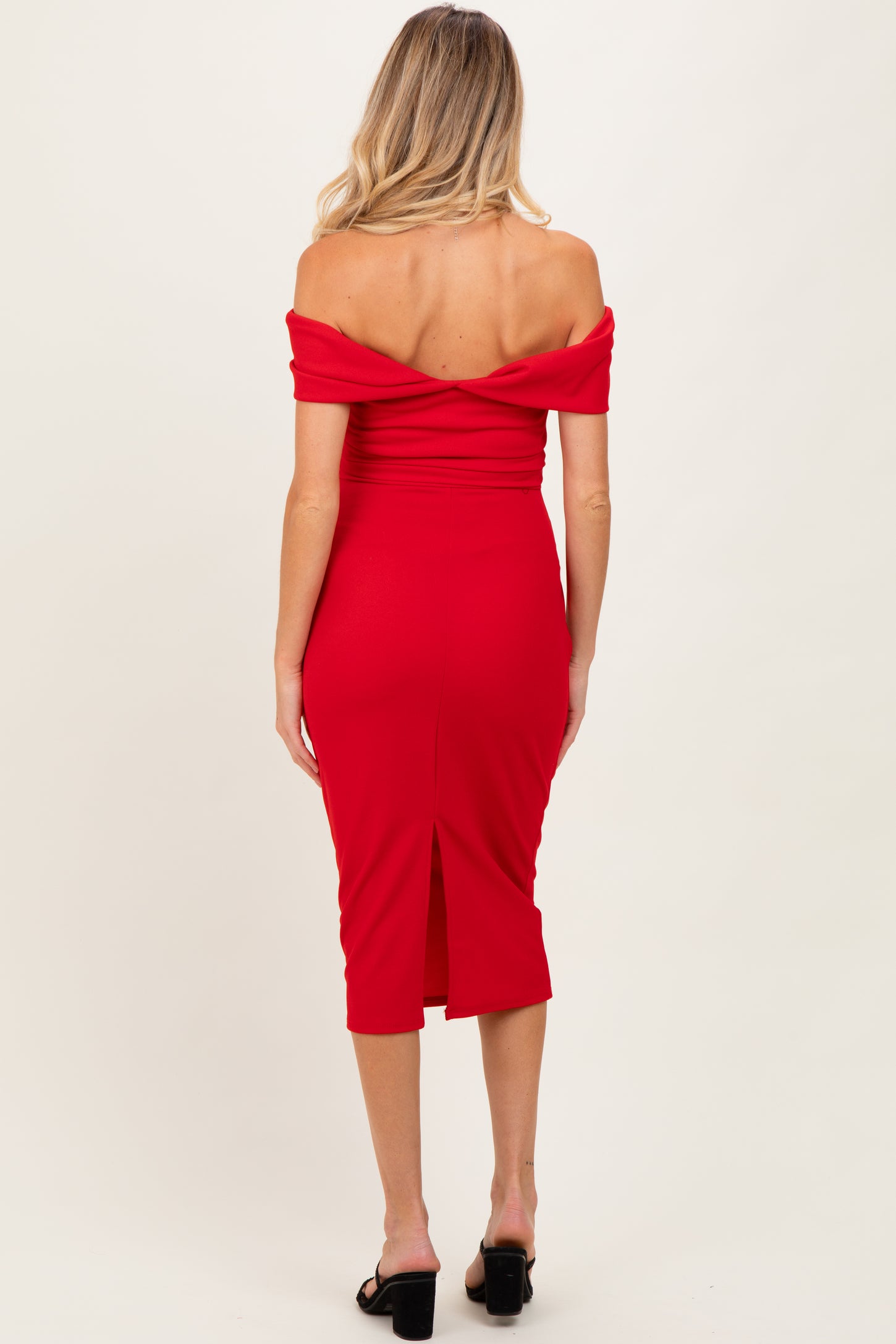 woman wearing a red off-the-shoulder maternity dress with a fitted silhouette and back slit, showing her baby bump