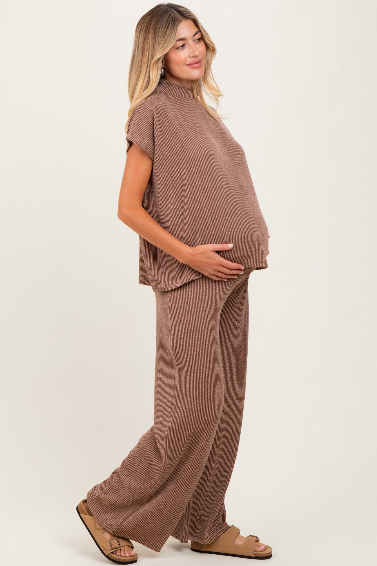 woman wearing a brown ribbed maternity outfit with a loose top and wide-leg pants, cradling her baby bump