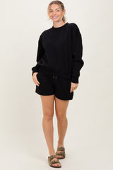 woman wearing a black oversized sweatshirt and black shorts, smiling with sandals on her feet