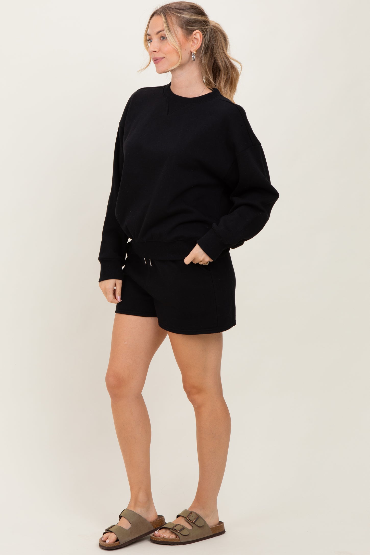 woman wearing a black oversized sweatshirt and black shorts with a drawstring, styled with casual slip-on sandals