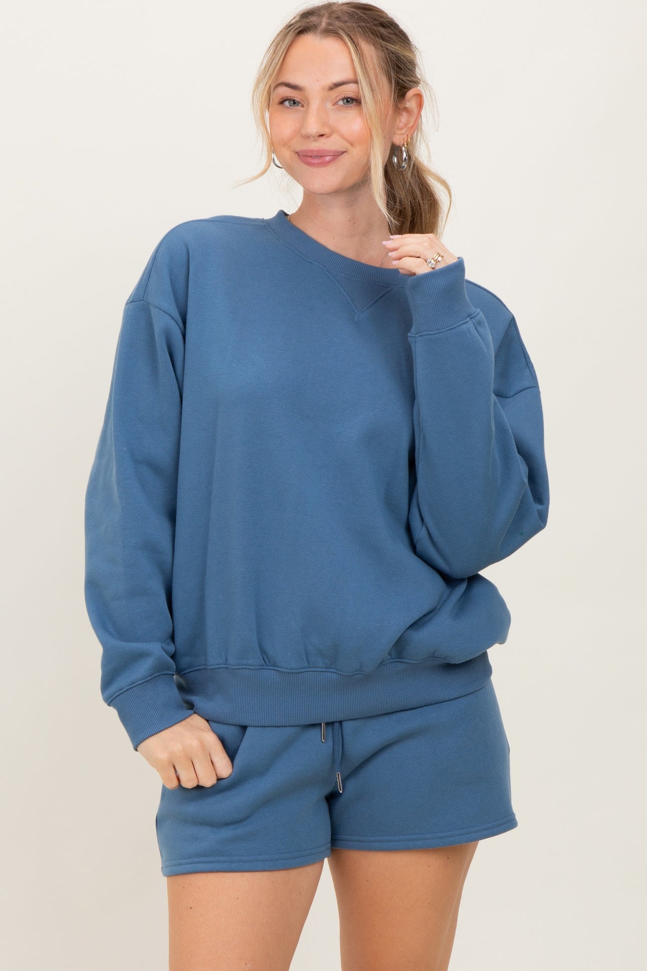 woman wearing a blue oversized sweatshirt with matching shorts, smiling at the camera