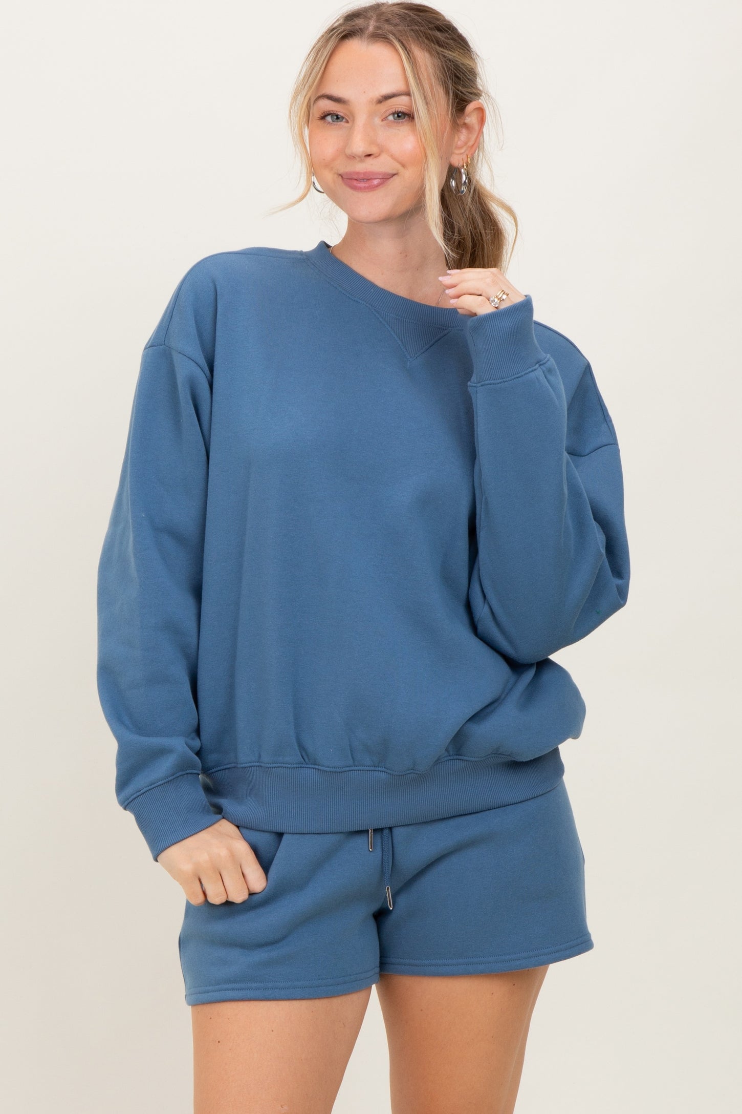 woman wearing a blue oversized sweatshirt with matching shorts, smiling at the camera
