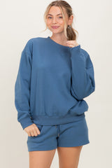 woman wearing a blue oversized sweatshirt with matching shorts, smiling at the camera