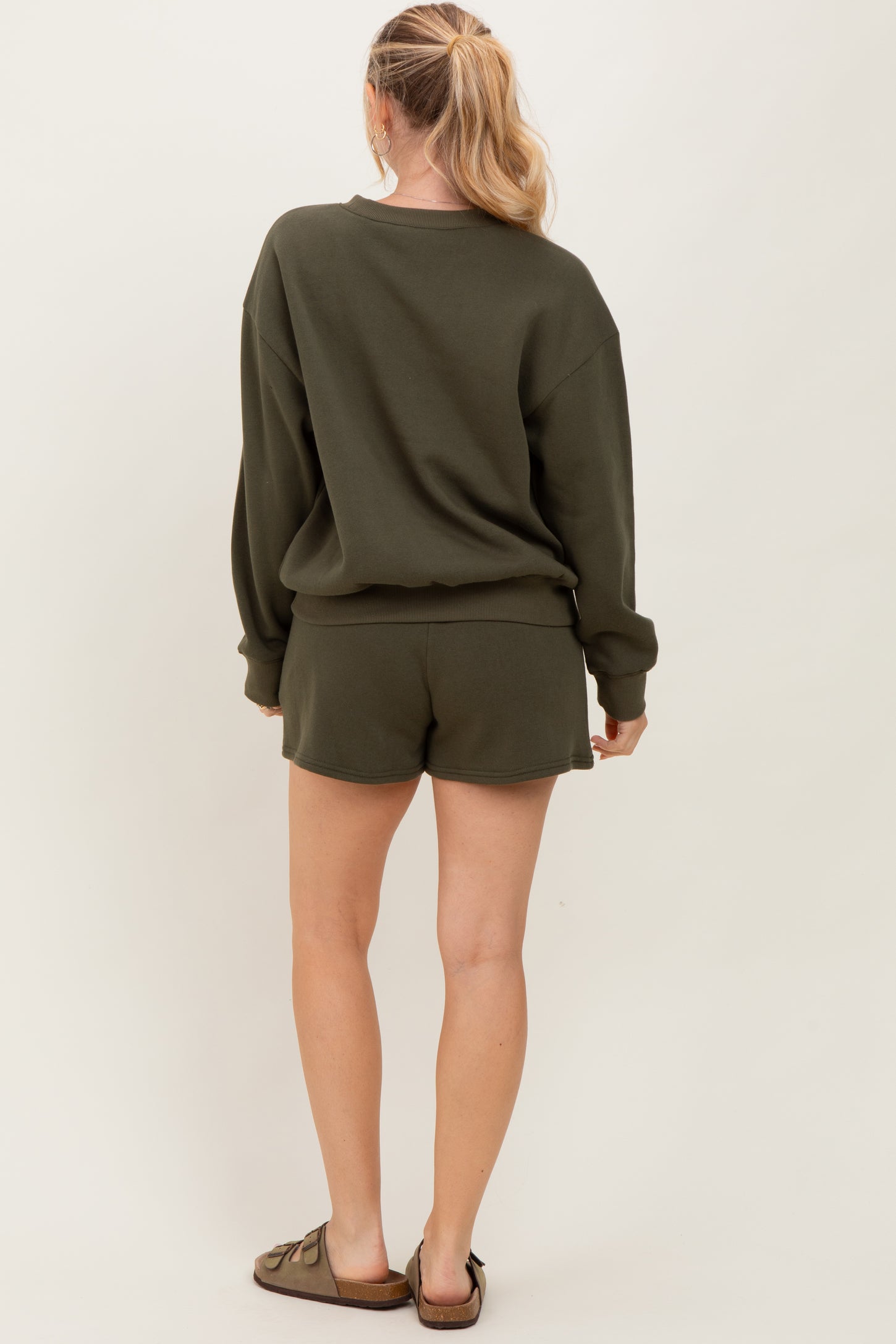 woman wearing an olive green oversized sweatshirt and matching shorts, seen from the back