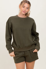 woman wearing a dark green oversized sweatshirt and matching shorts, smiling at the camera