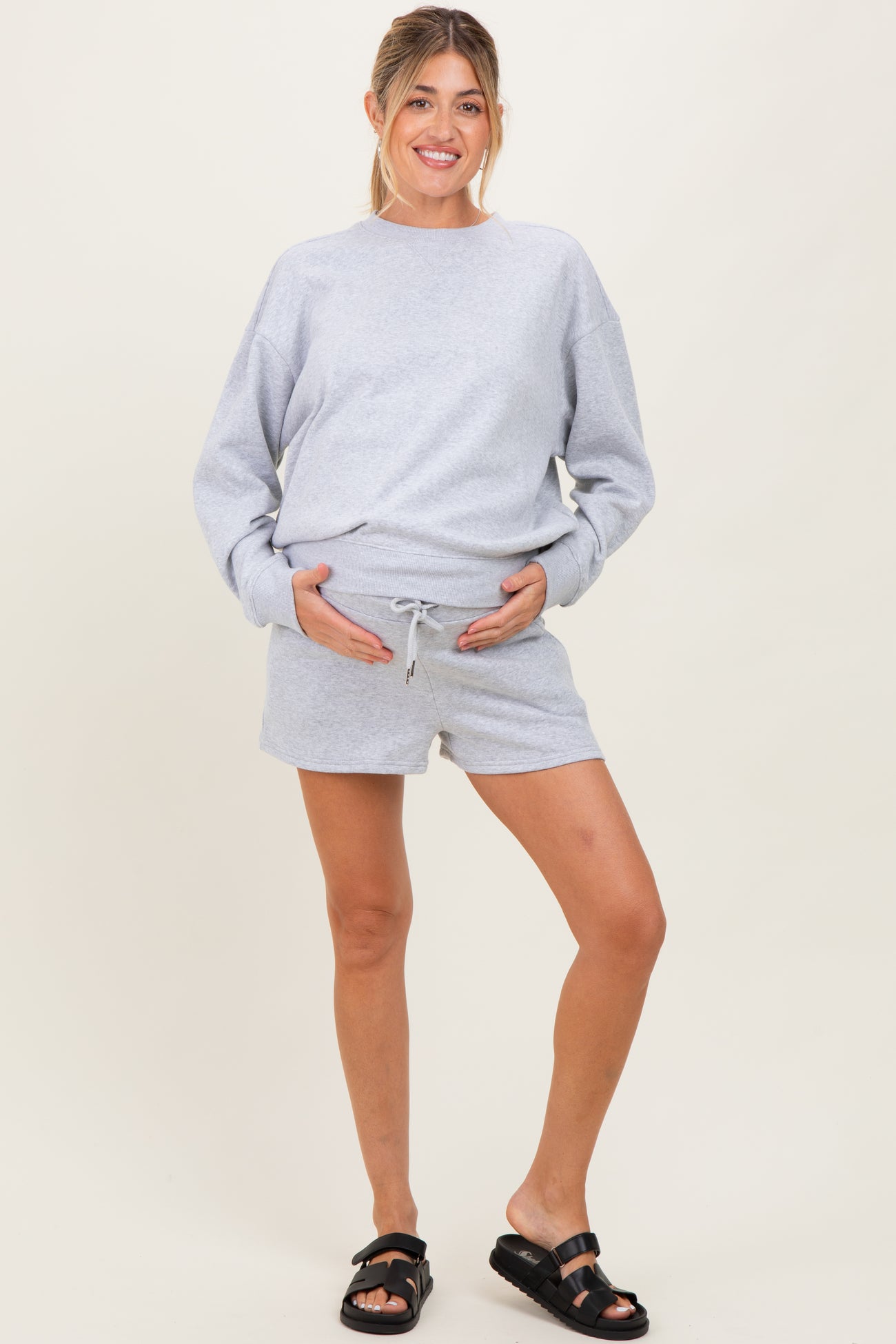 woman wearing a grey maternity sweatshirt and matching shorts, holding her baby bump
