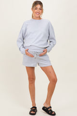 woman wearing a grey maternity sweatshirt and matching shorts, holding her baby bump