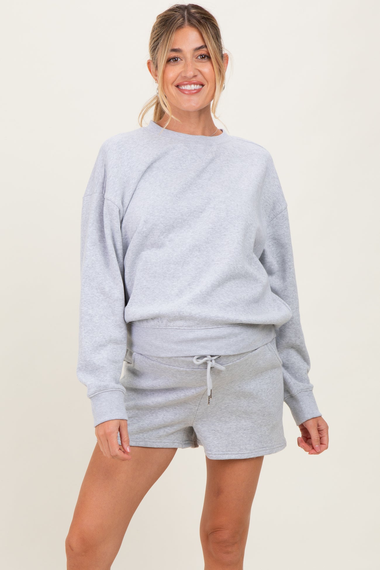 woman wearing a light grey maternity sweatshirt and matching maternity shorts with a drawstring waist