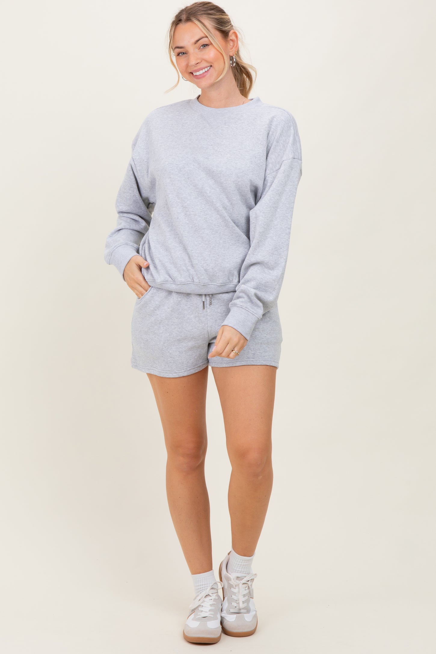 woman wearing a gray sweatshirt and matching shorts, posing with one hand in pocket and smiling