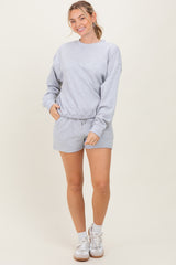 woman wearing a gray sweatshirt and matching shorts, posing with one hand in pocket and smiling
