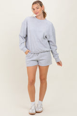 woman wearing a gray sweatshirt and matching shorts with a drawstring waist, standing with one hand in the pocket