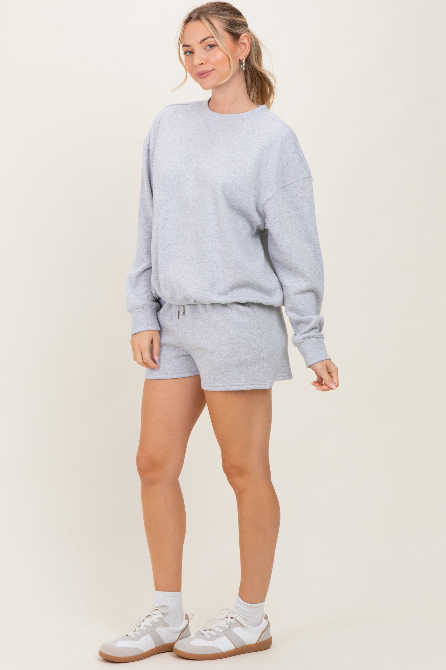 woman wearing a gray oversized sweatshirt and matching shorts with a relaxed fit and white sneakers