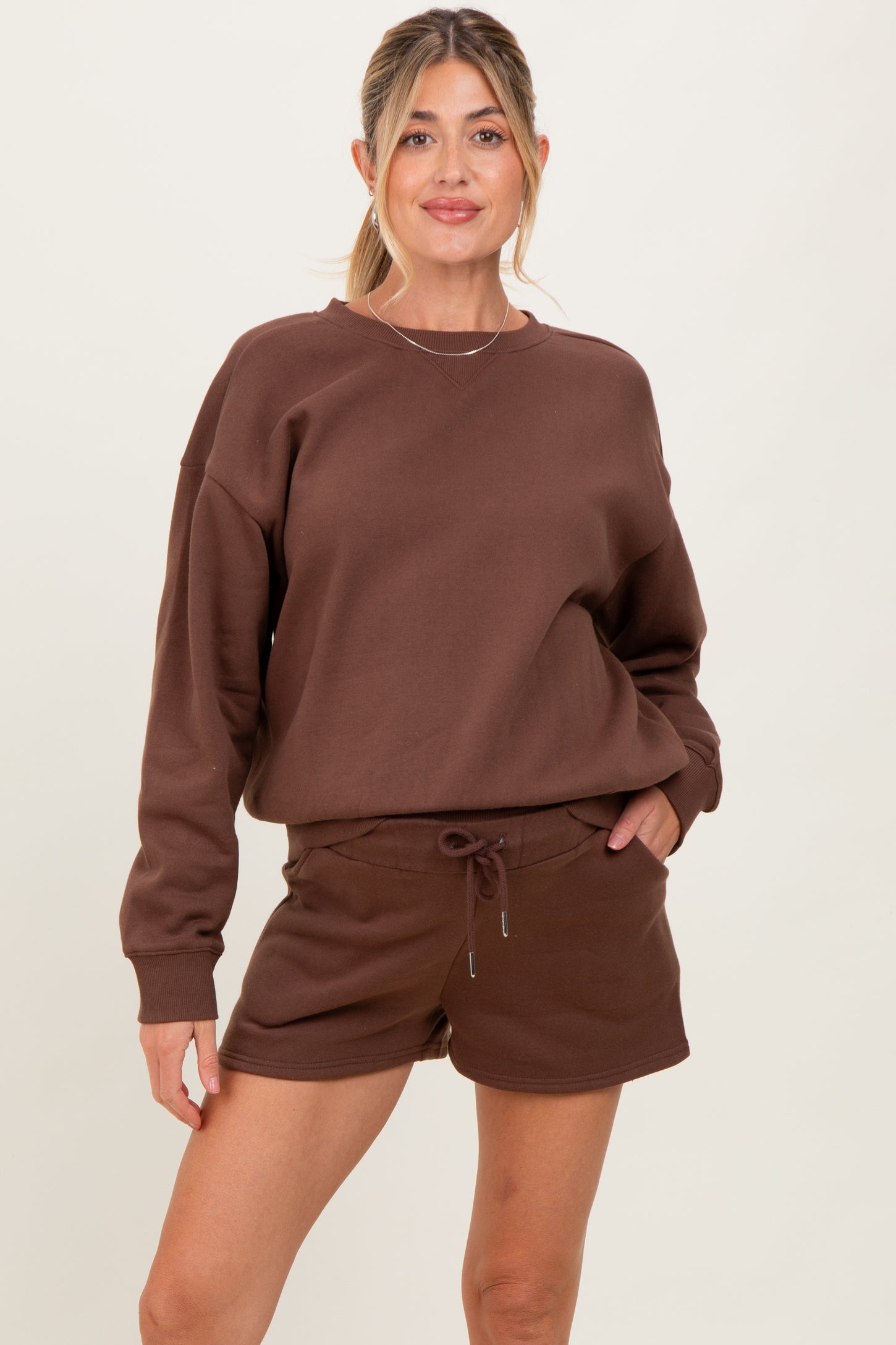 woman wearing a brown maternity sweatshirt and matching shorts, smiling at the camera