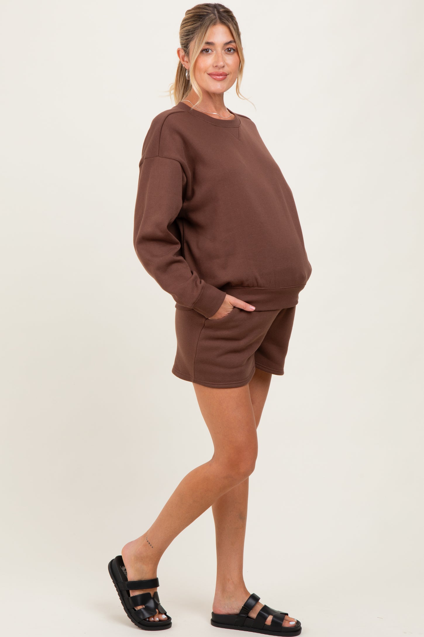 woman wearing a brown maternity sweatshirt and matching shorts with pockets, showcasing her baby bump