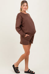 woman wearing a brown maternity sweatshirt and matching shorts with pockets, showcasing her baby bump
