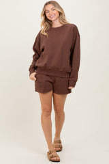 woman wearing a brown oversized sweatshirt and matching shorts, standing casually with one hand in her pocket