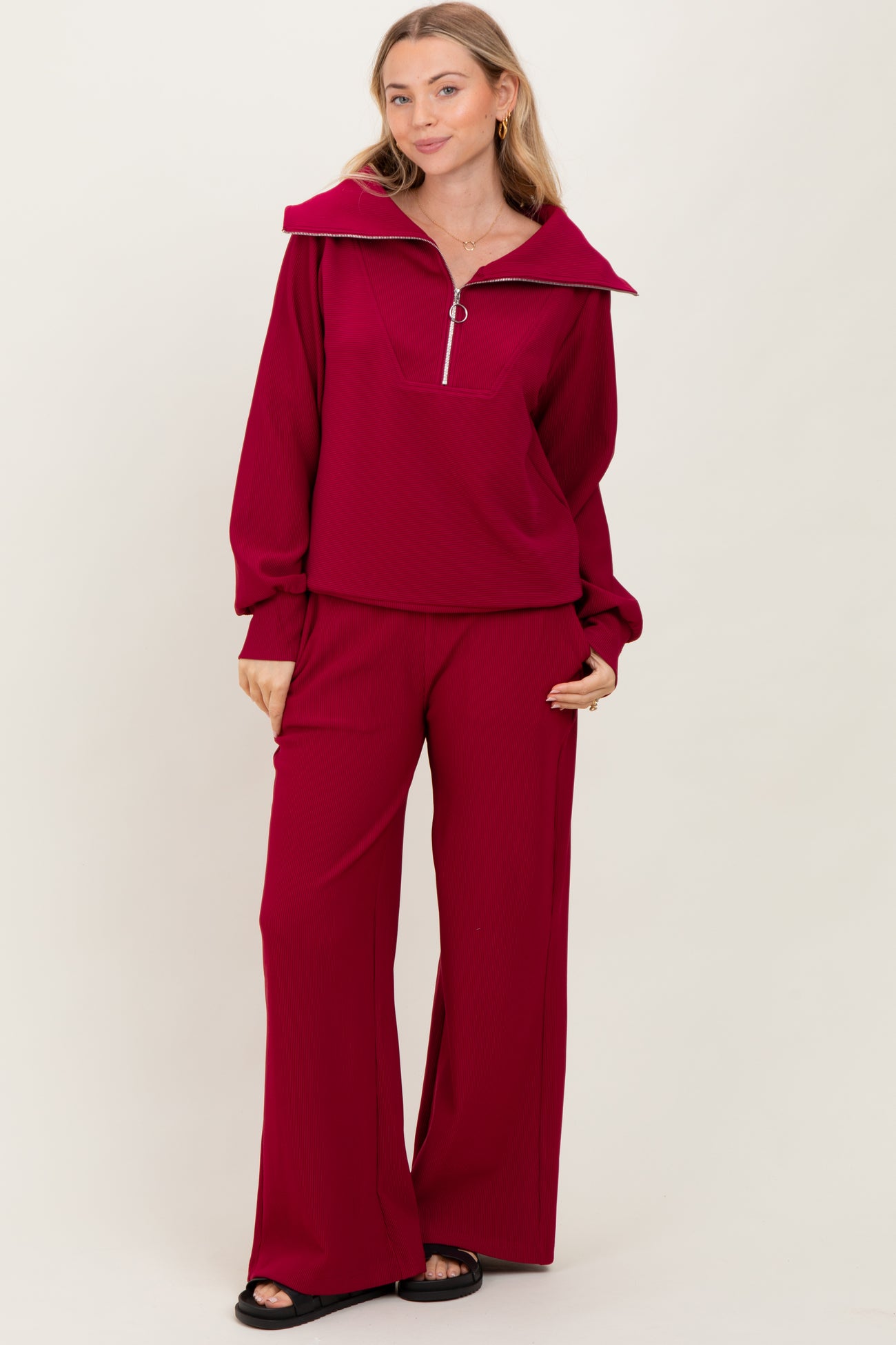 woman wearing a deep red long sleeve zip-up top with wide collar and matching wide-leg pants