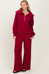 woman wearing a deep red long sleeve zip-up top with wide collar and matching wide-leg pants