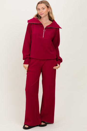 woman wearing a deep red long sleeve zip-up top with wide collar and matching wide-leg pants