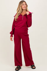woman wearing a burgundy maternity loungewear set with a zip-up top and wide-leg pants