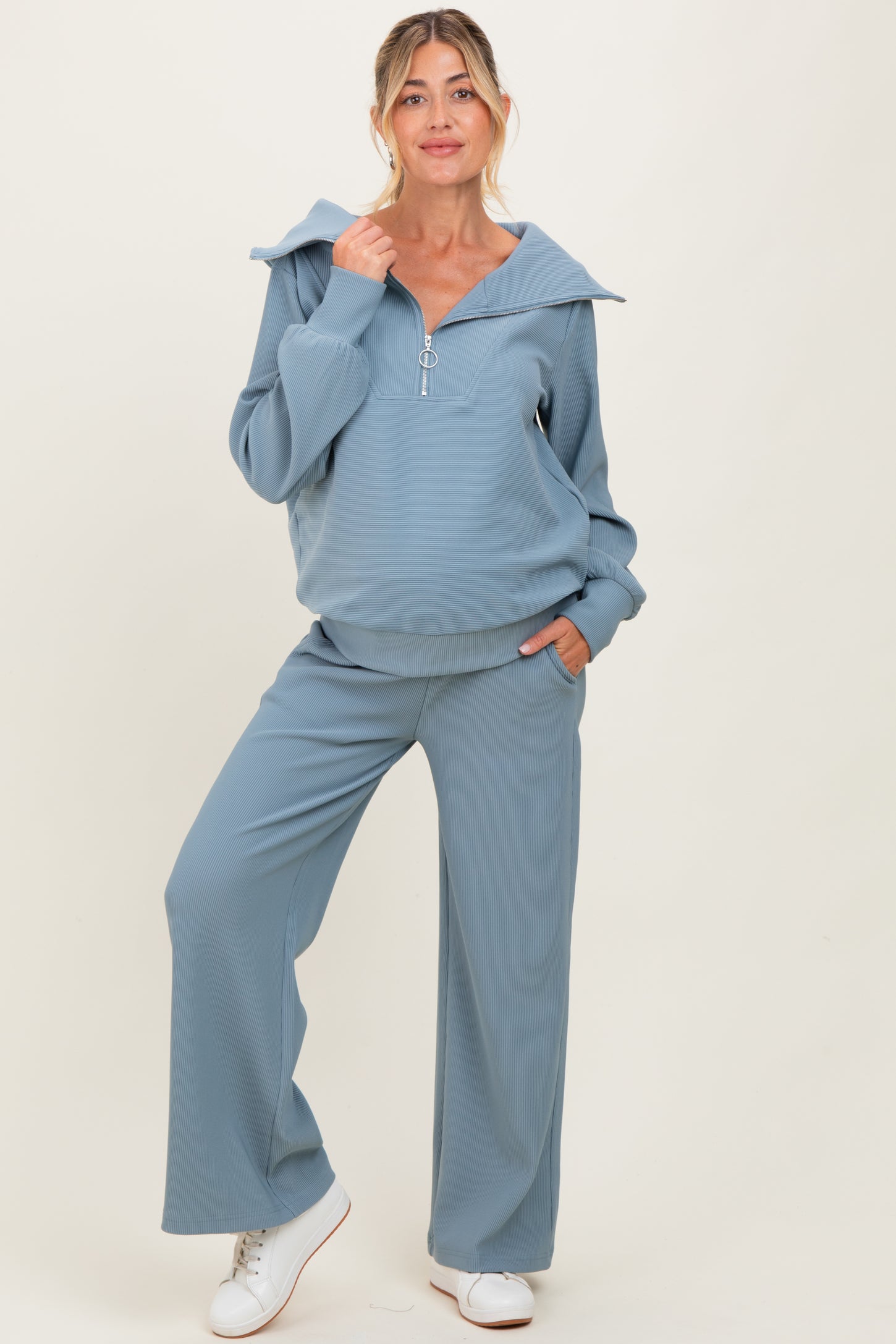 woman wearing a light blue maternity loungewear set with a hoodie and wide-leg pants, showing a baby bump