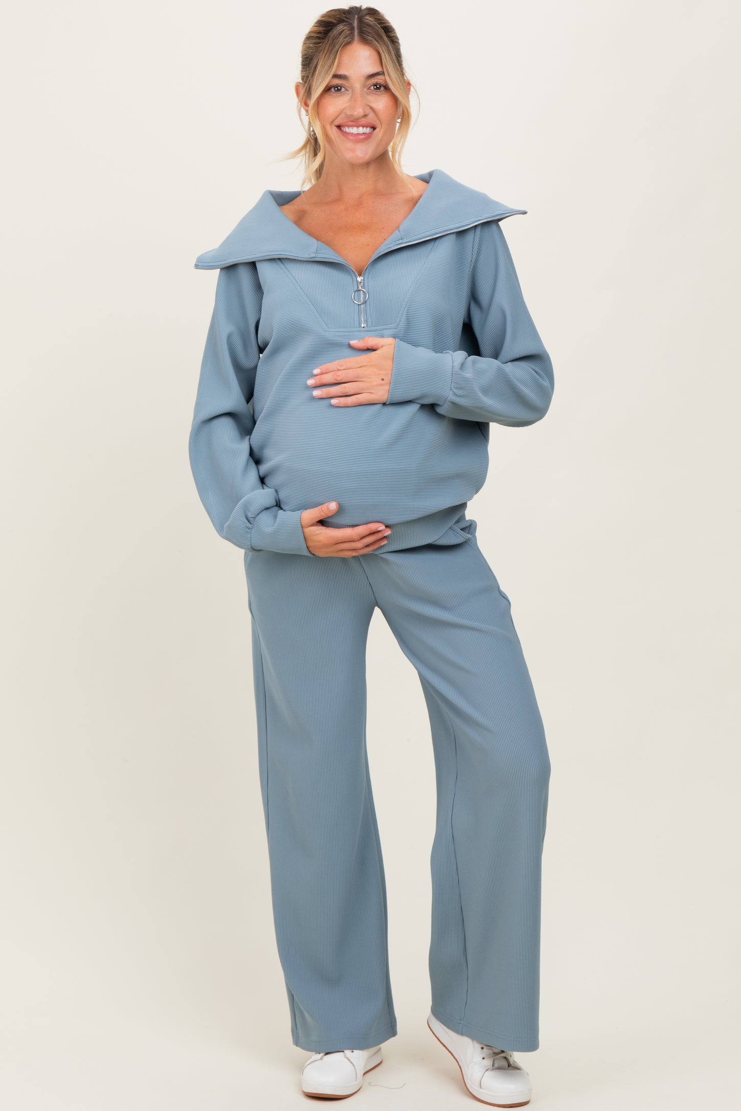 woman wearing a light blue maternity tracksuit with a zip-up top and wide-leg pants, showcasing her baby bump