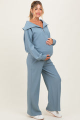 woman wearing a light blue maternity tracksuit with a zip-up hooded top and matching pants, holding her baby bump