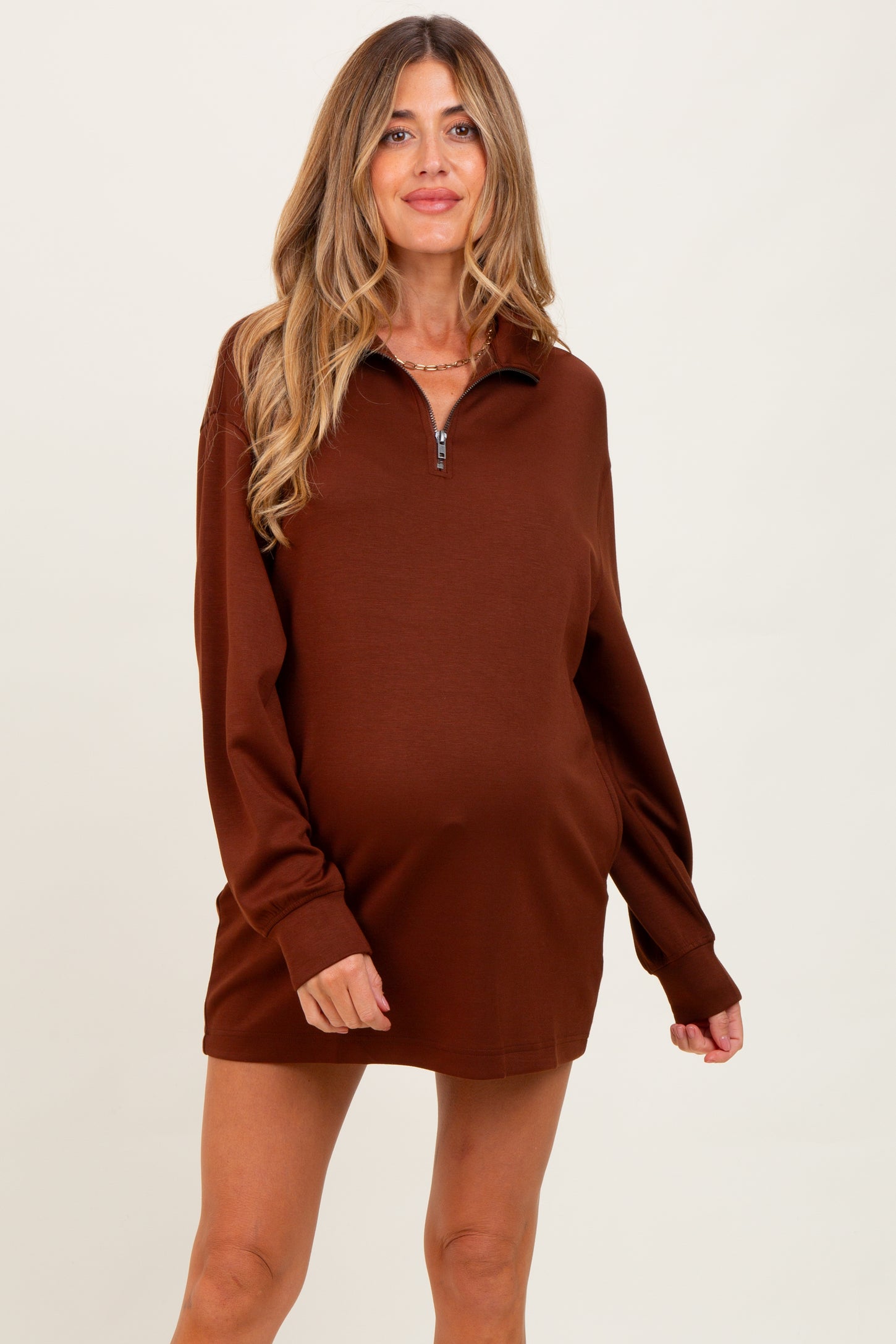 woman wearing a brown maternity zip-up sweatshirt dress and showing her baby bump